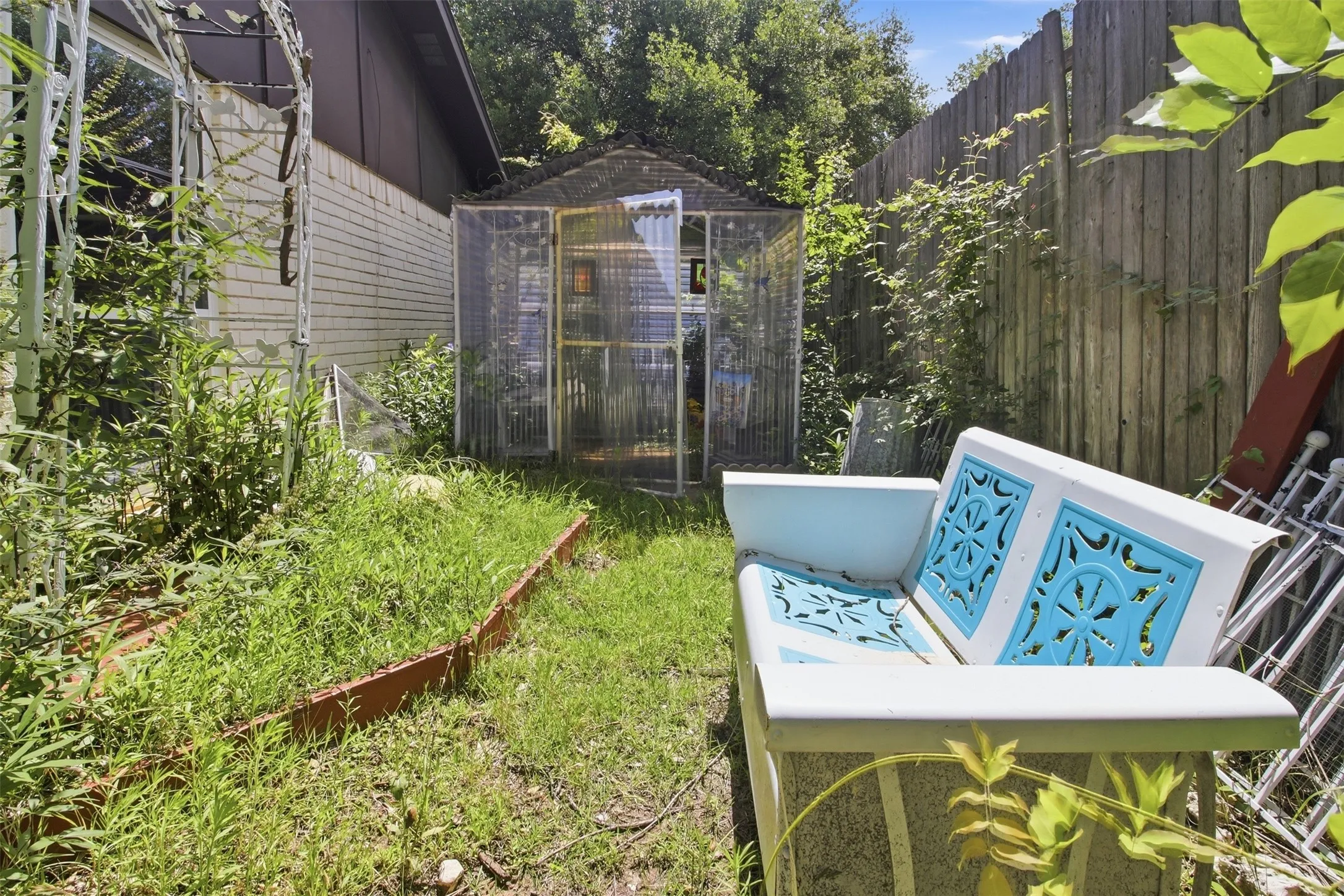 Outdoor area featuring a greenhouse structure, a wood fence, and a brick exterior wall