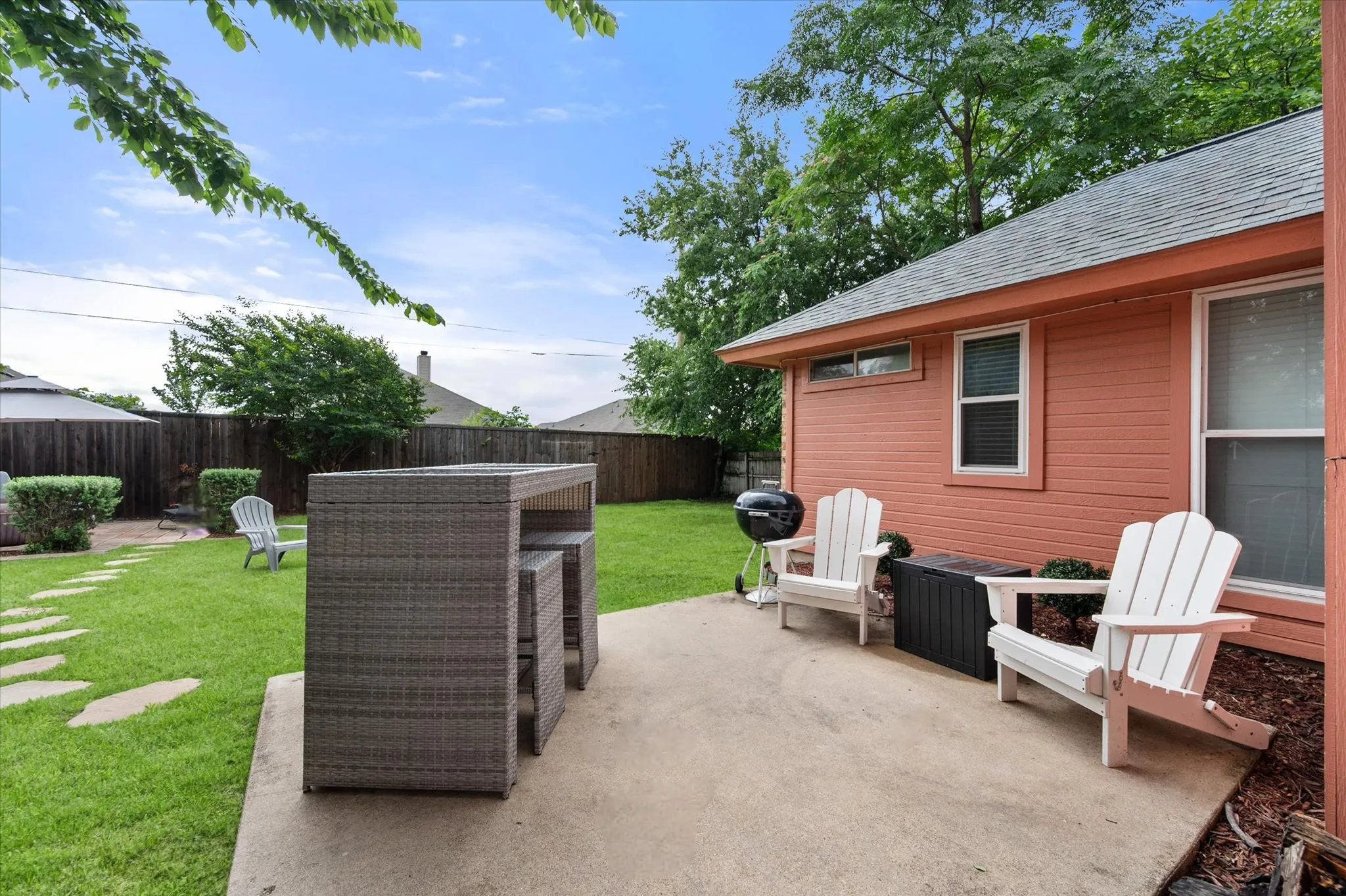 Manicured backyard featuring a concrete patio, wood privacy fencing, and mature trees