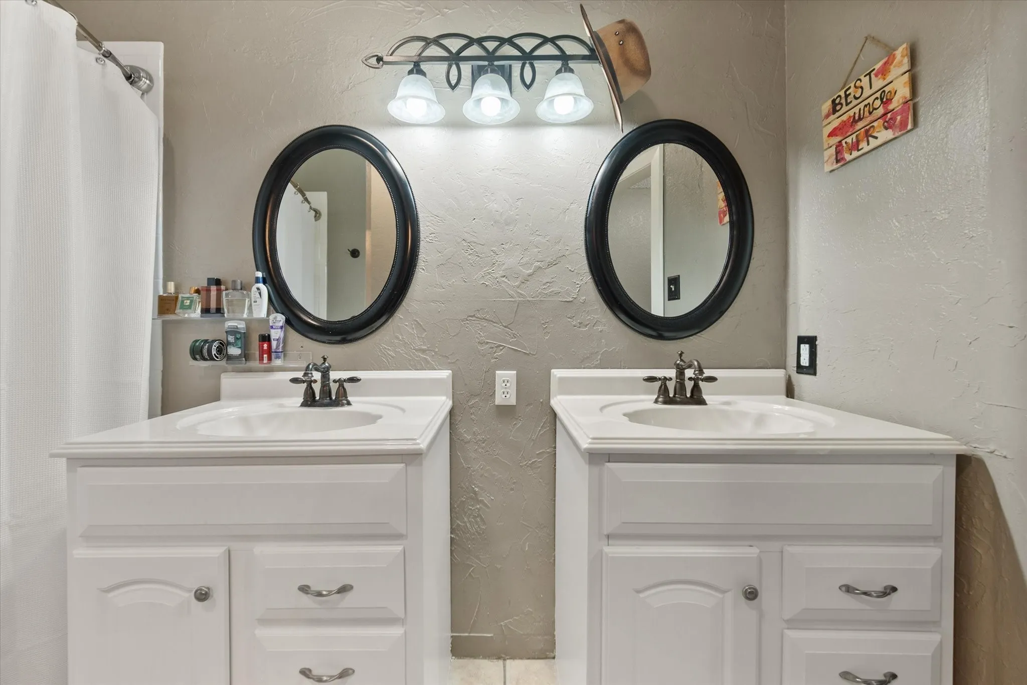 Dual vanity sinks with white cabinetry, oval framed mirrors, and a three-light fixture
