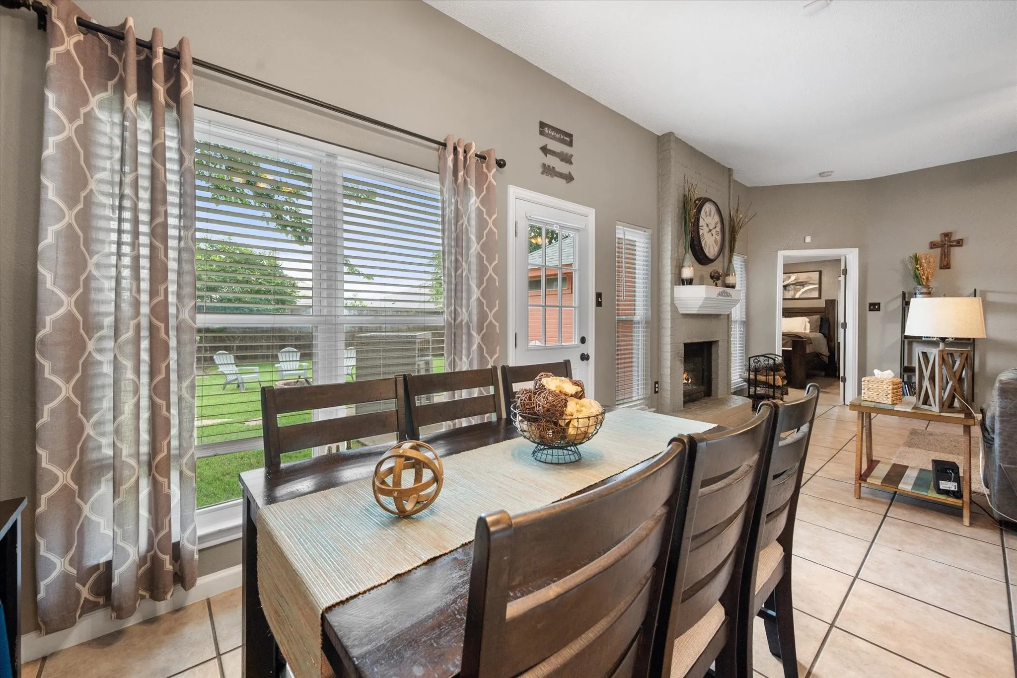 Dining area featuring tile flooring, a large window with blinds, a white door leading outdoors, and a built-in fireplace with a mantel
