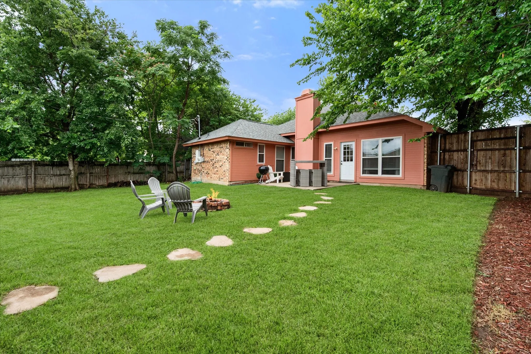 Expansive backyard featuring a large grass area, stepping stones, wood fencing, and mature trees