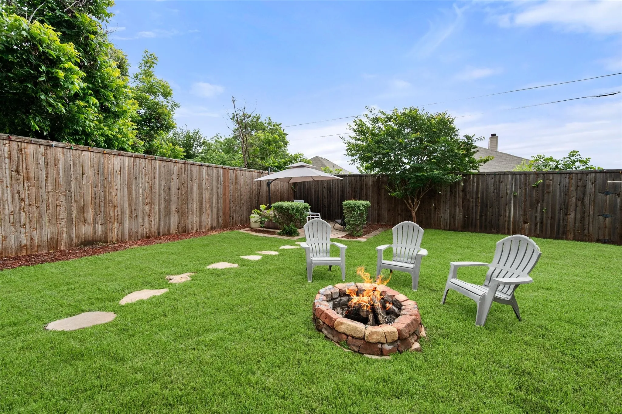 Expansive backyard featuring a stone-lined fire pit, a manicured lawn, and a privacy fence