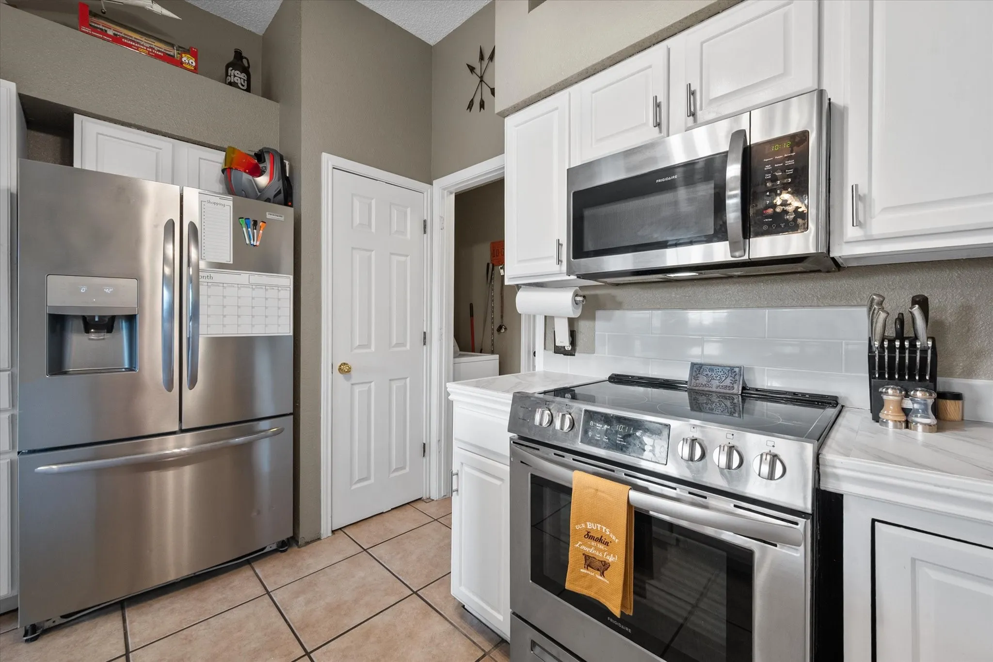 Kitchen featuring white cabinetry, stainless steel appliances, subway tile backsplash, and tile flooring