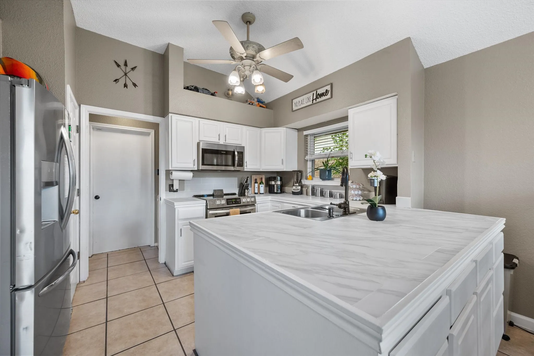 Kitchen featuring white cabinetry, stainless steel appliances, a ceiling fan, a kitchen island with a double basin sink, and tile flooring