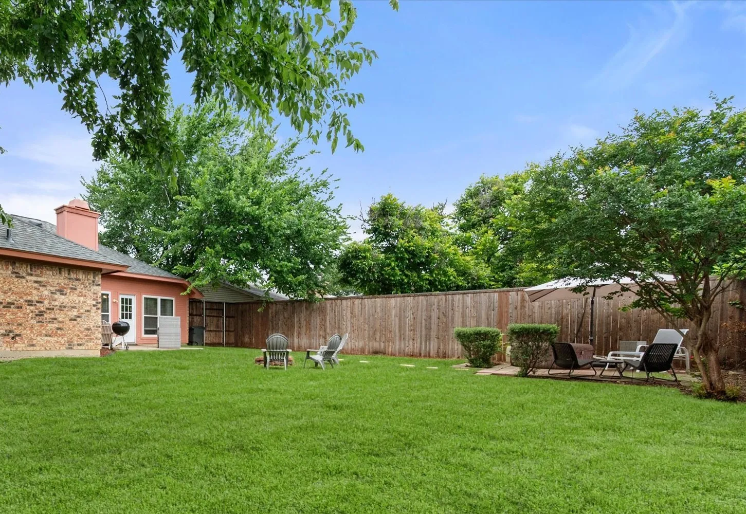 Spacious backyard featuring a manicured lawn, a full privacy fence, mature trees, and a brick exterior home with a back patio door