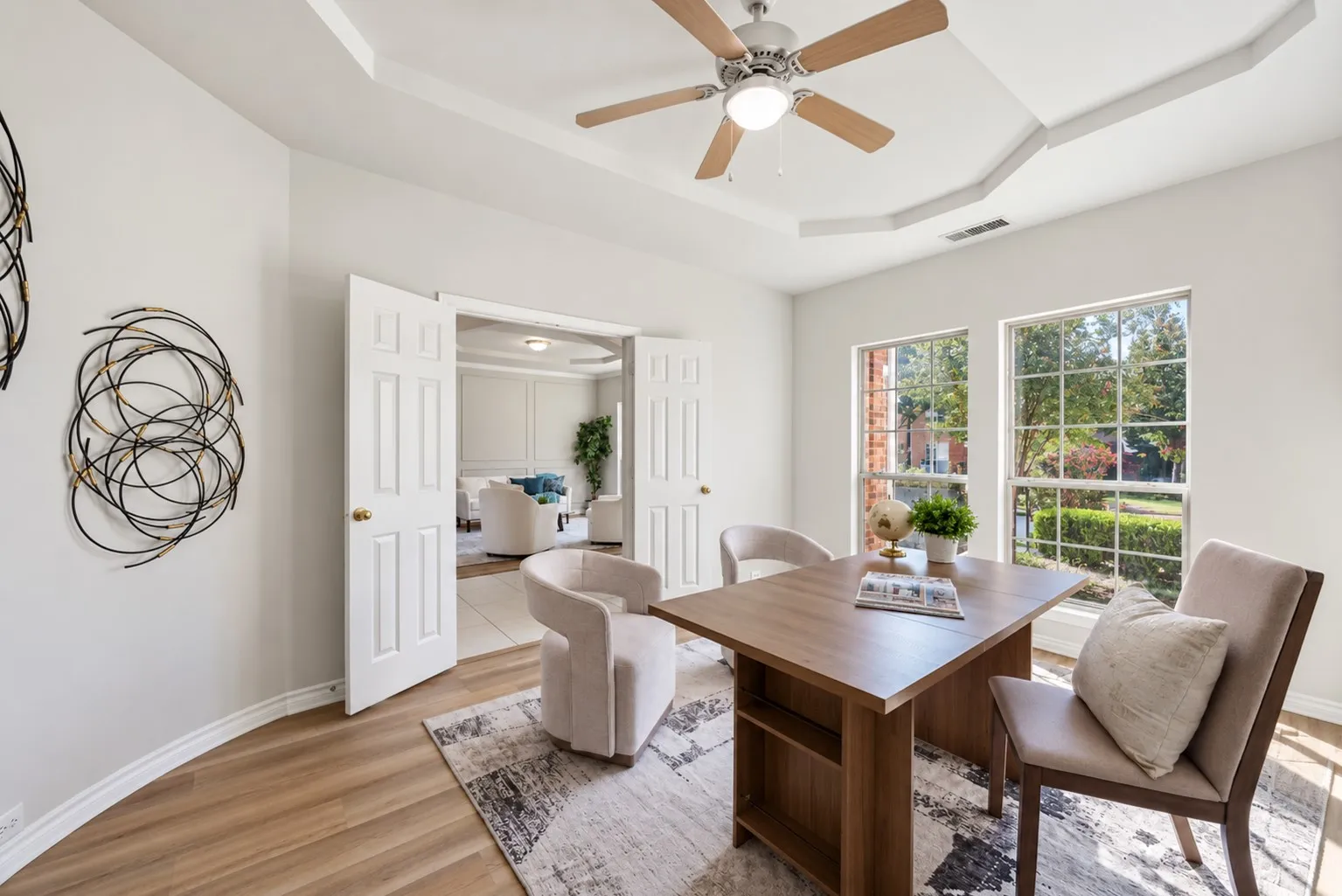 Wood-finish flooring, tray ceiling, ceiling fan with light, French doors, and two large windows