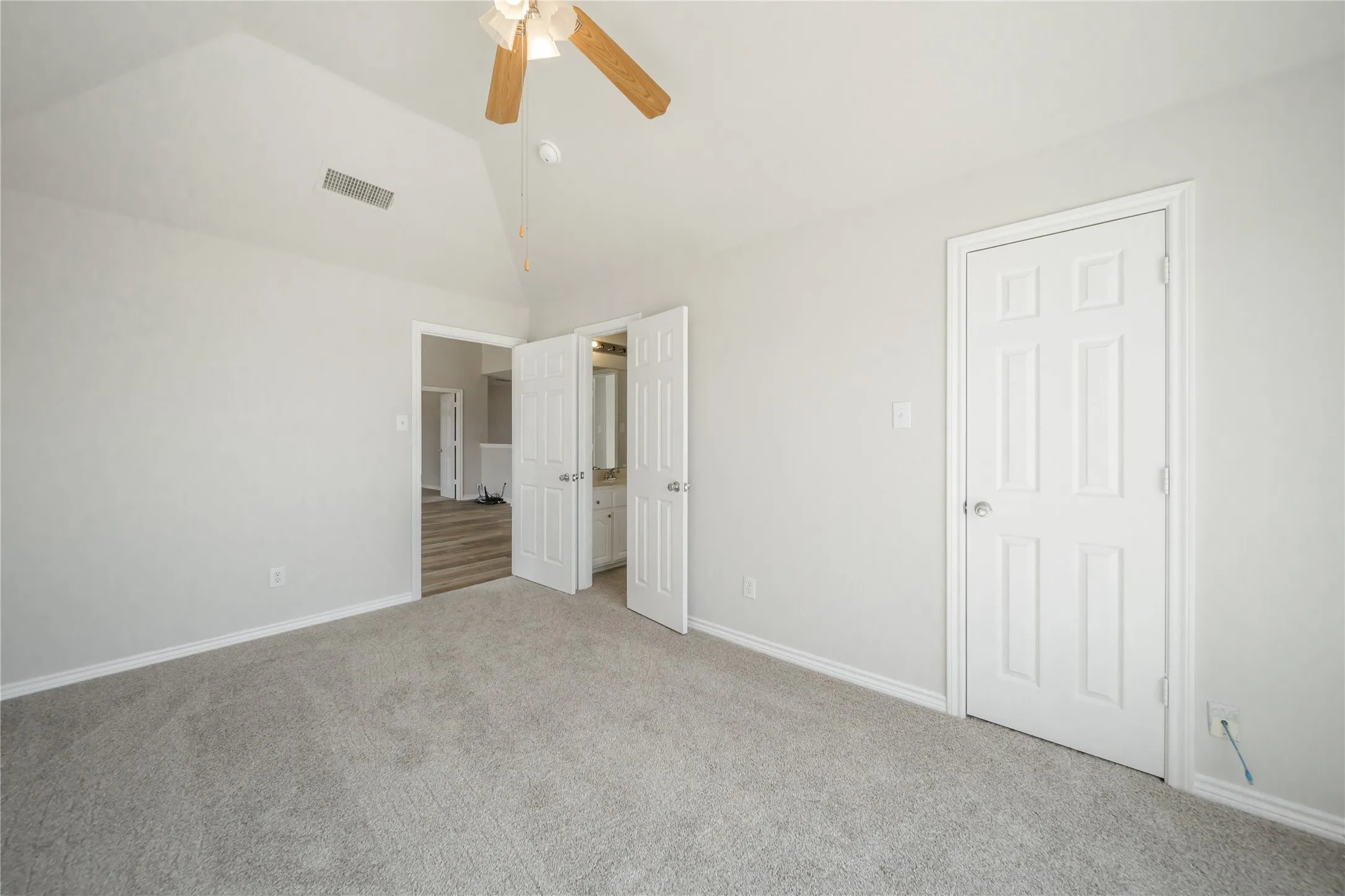 Carpeted room with a vaulted ceiling and a wood-bladed ceiling fan
