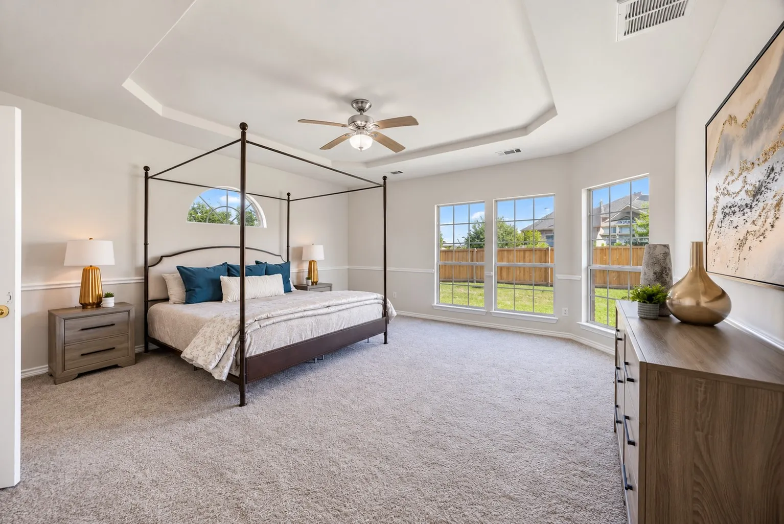 Tray ceiling with a ceiling fan, arched transom window, large windows with gridded panes, and carpeted flooring