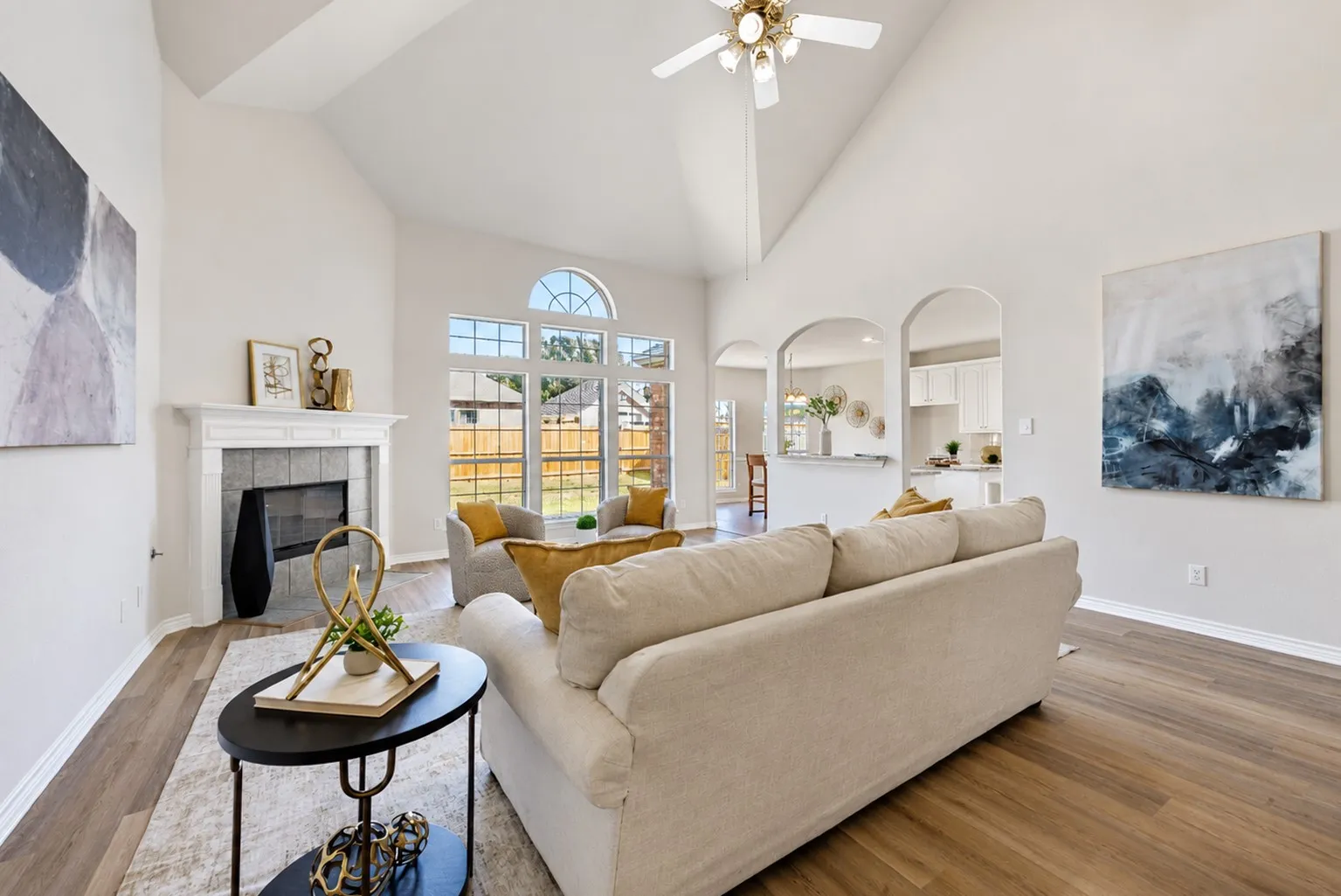 Vaulted ceiling with a ceiling fan, fireplace with a mantel, arched doorways, wood-finish flooring, and large windows