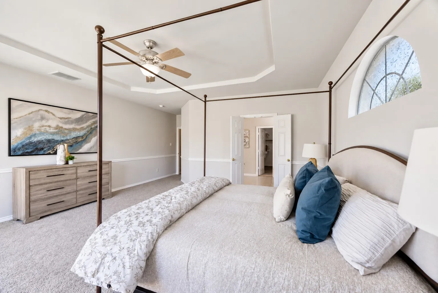 Carpeted bedroom featuring a tray ceiling, ceiling fan with light, arched window, and double doors