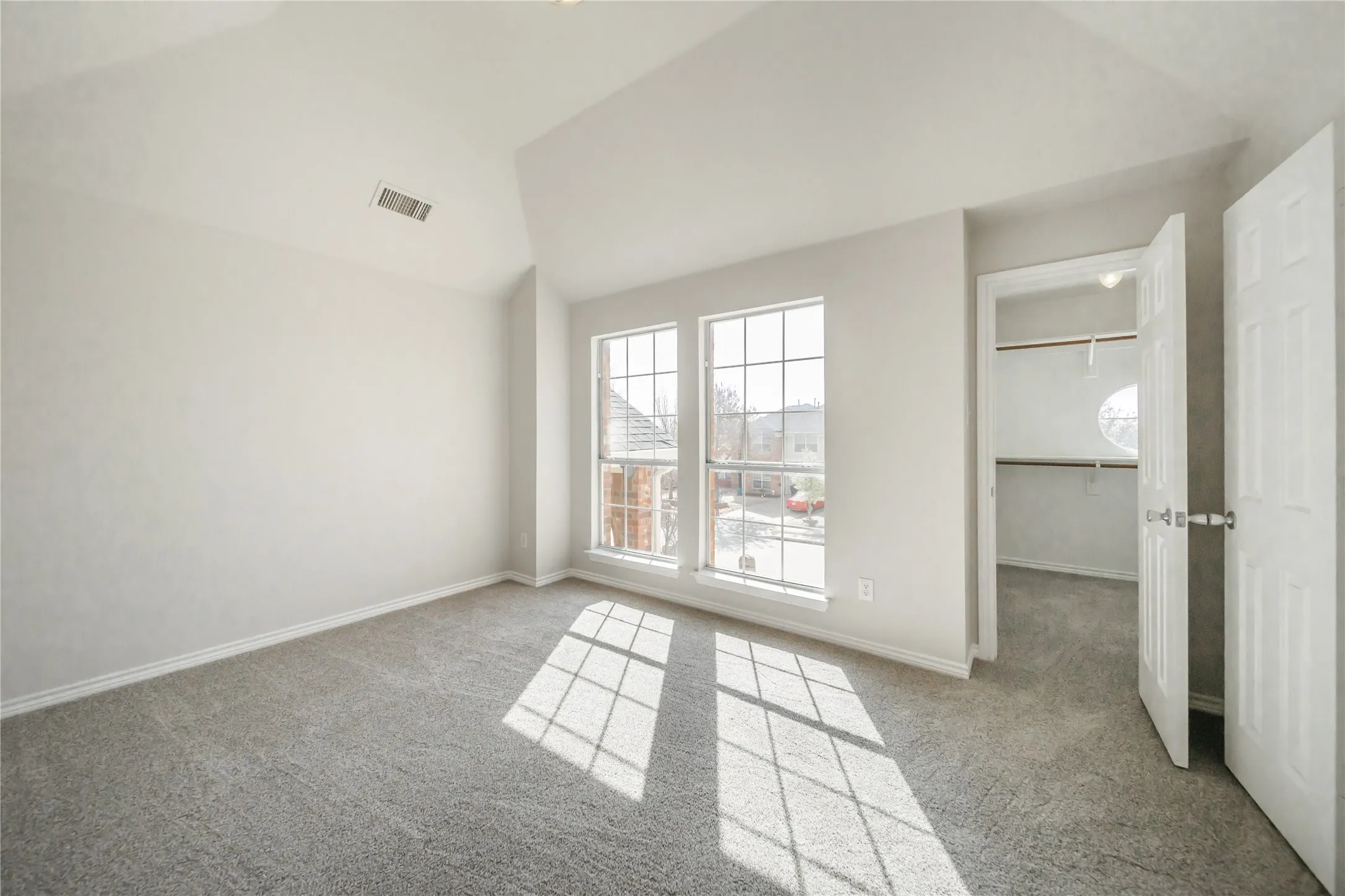 Room featuring light gray carpeting, vaulted ceilings, and two large windows with grid patterns