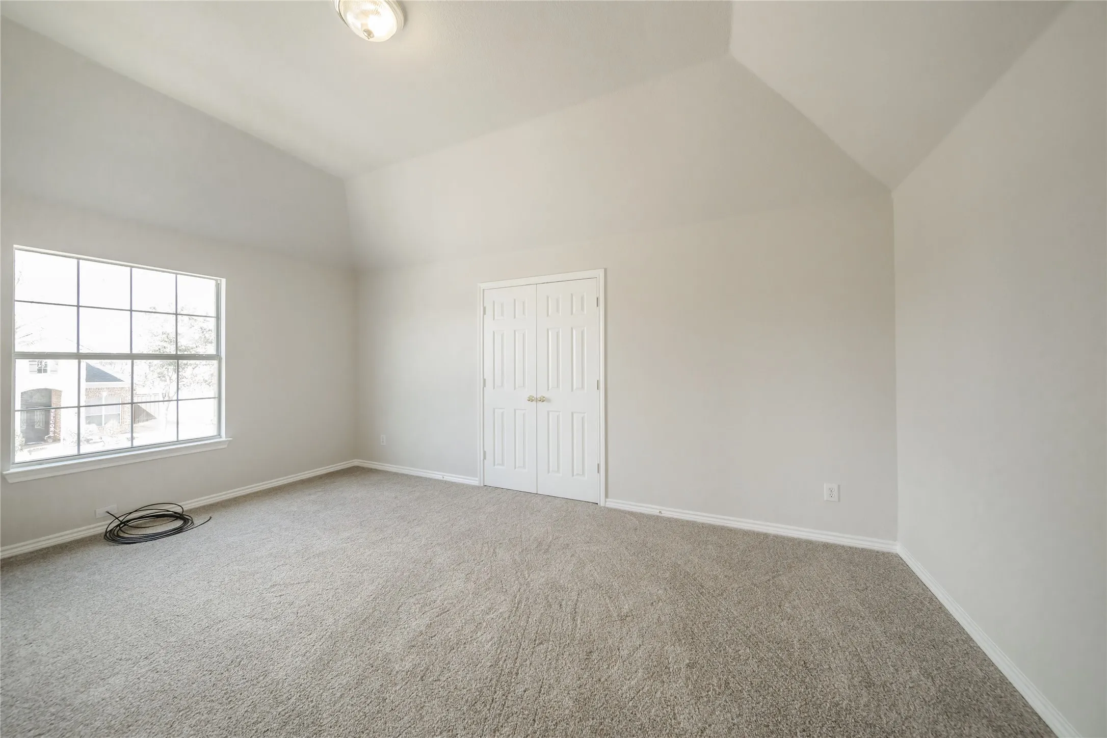 Spacious interior room featuring vaulted ceilings, neutral-toned carpeting, and a large multi-pane window