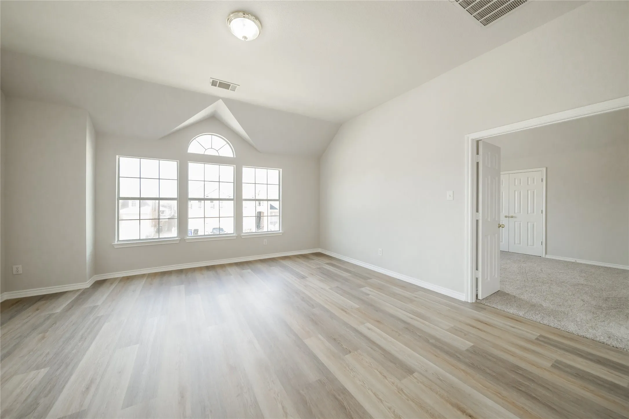 Room featuring wood-finish flooring, vaulted ceiling, and a large window array with an arched transom
