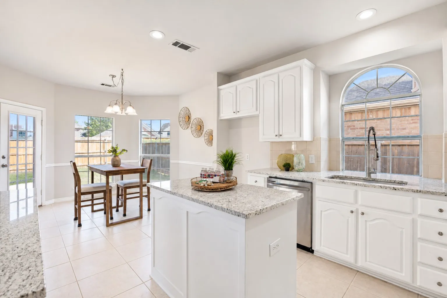 White cabinetry with granite countertops, stainless steel appliances, tile flooring, and an arched window above the sink