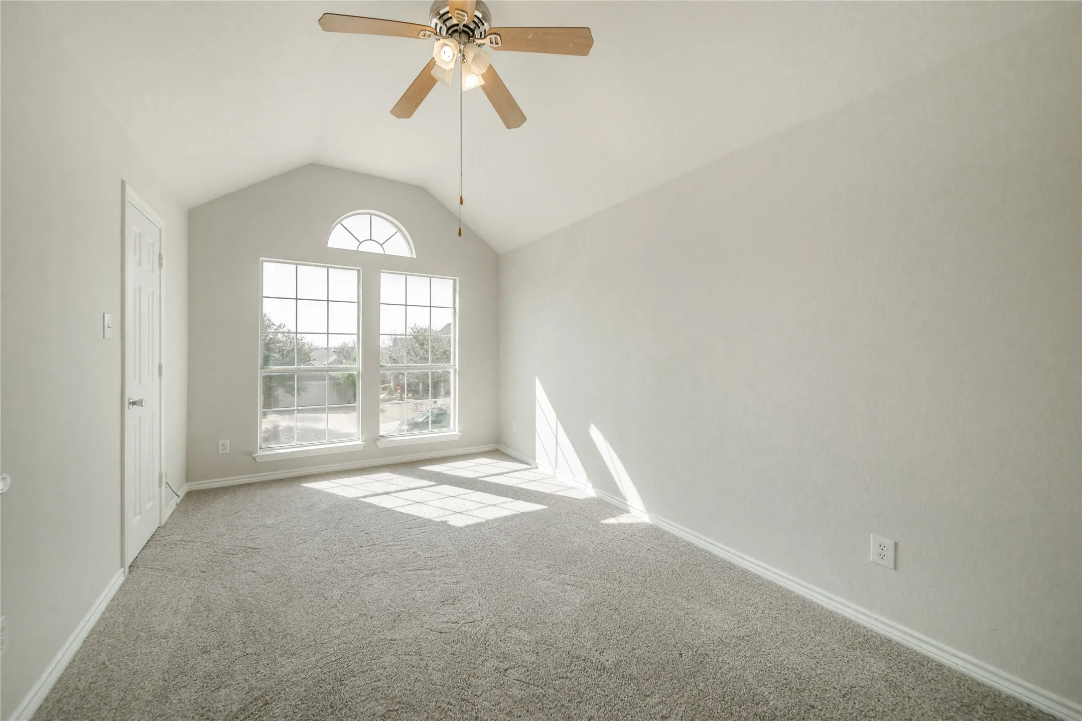 Vaulted ceiling room featuring a large arched window, two vertical windows, a ceiling fan with integrated lighting, and neutral-toned carpeting