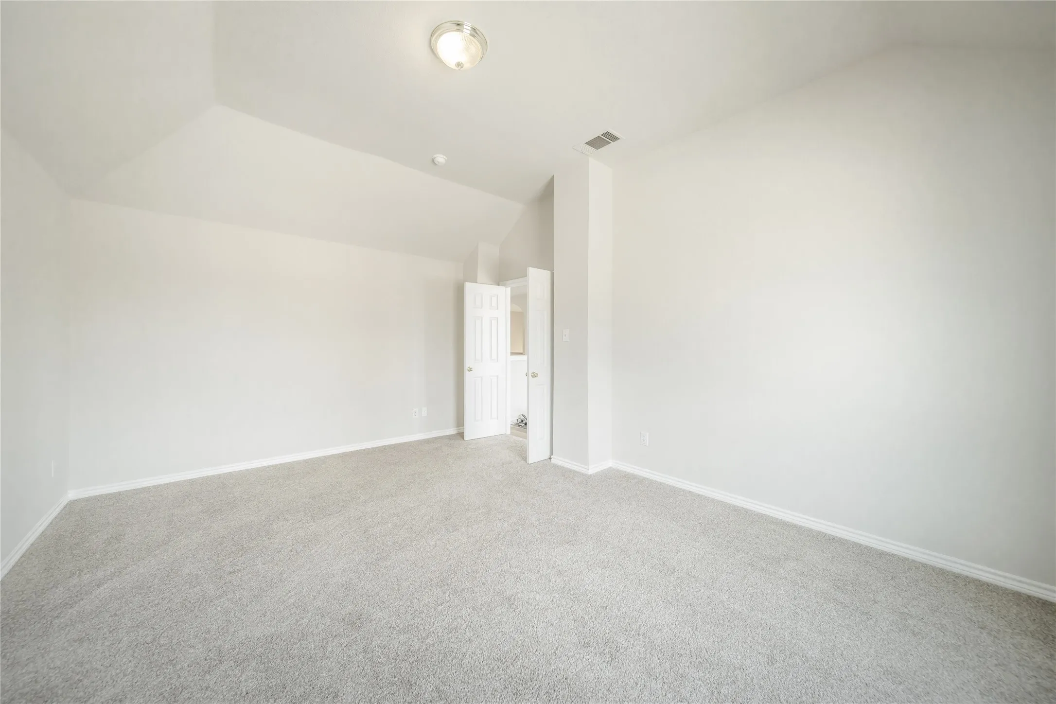 Spacious room featuring vaulted ceilings, light gray carpeting, and white baseboards