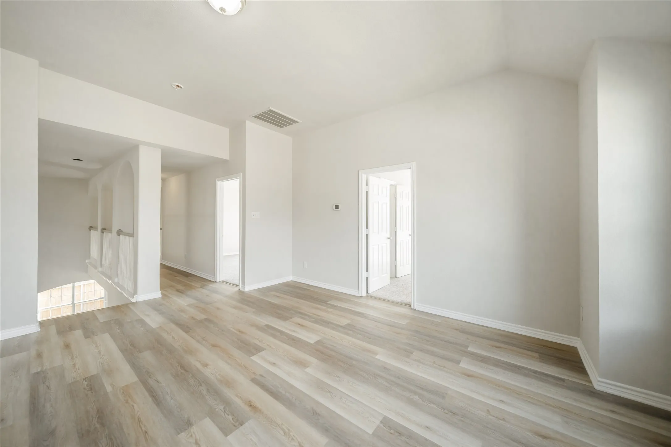 Spacious room featuring wood-finish flooring, vaulted ceiling, and neutral wall tones