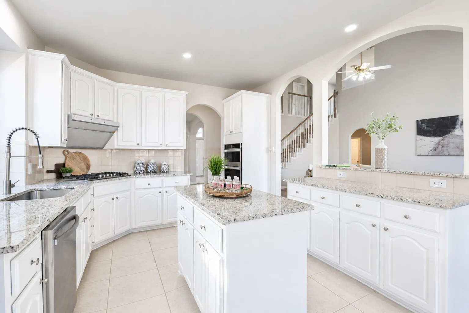 White cabinetry with silver-tone hardware, granite countertops, tile flooring, built-in stainless steel appliances, and architectural archways