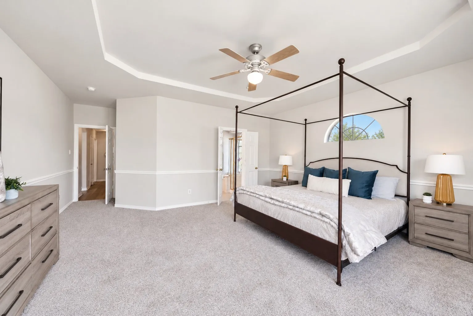 Tray ceiling with crown molding, ceiling fan, arched window, and neutral carpeting