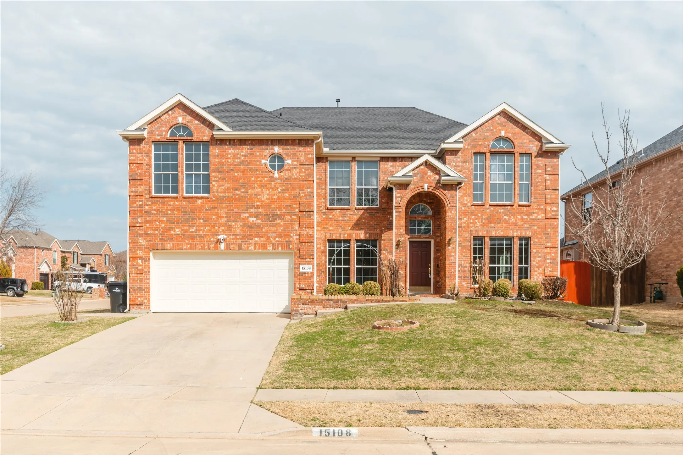 Traditional-style brick home featuring a two-car garage, arched entry with a dark wood door, gabled rooflines, and multiple large windows