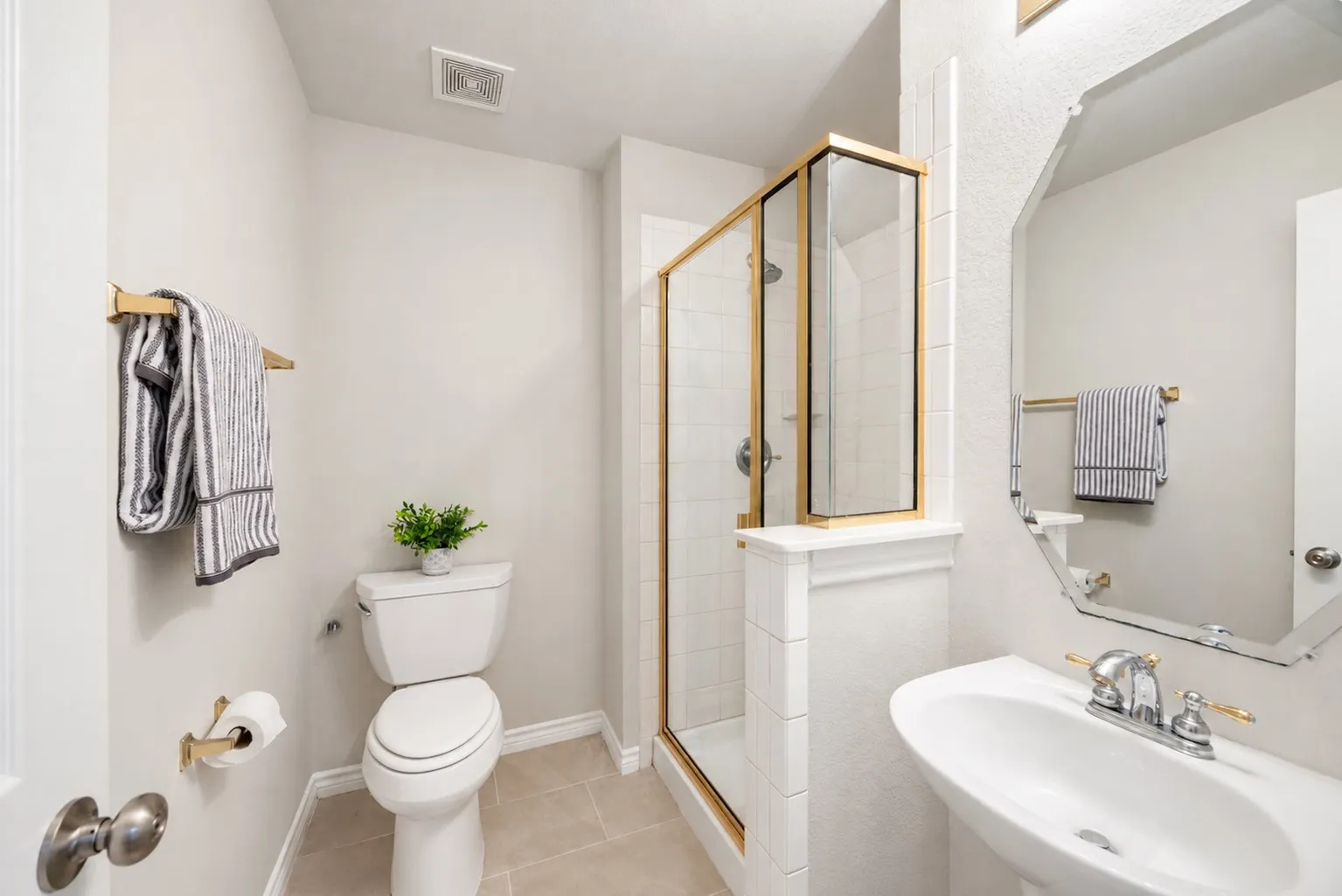 Pedestal sink with chrome and gold-tone fixtures, geometric mirror, and shower with a gold-tone framed enclosure
