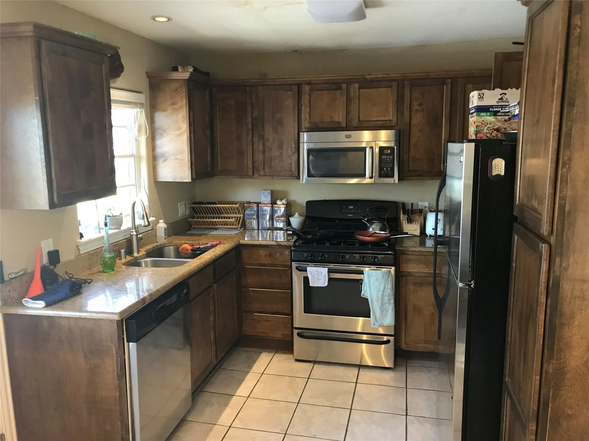 Kitchen featuring wood cabinetry, light-toned countertops, stainless steel appliances, and tile flooring