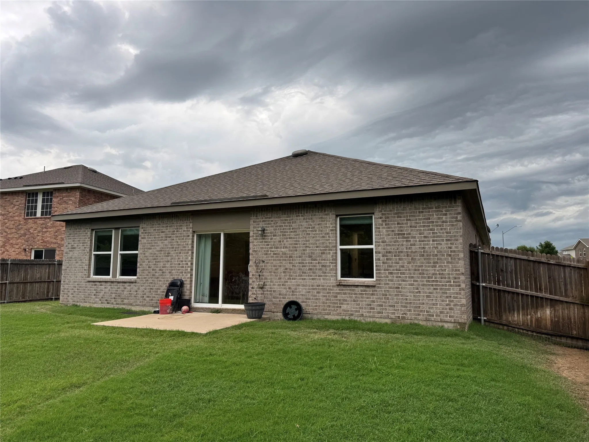 Expansive grassy backyard featuring a concrete patio, brick exterior, and a privacy fence