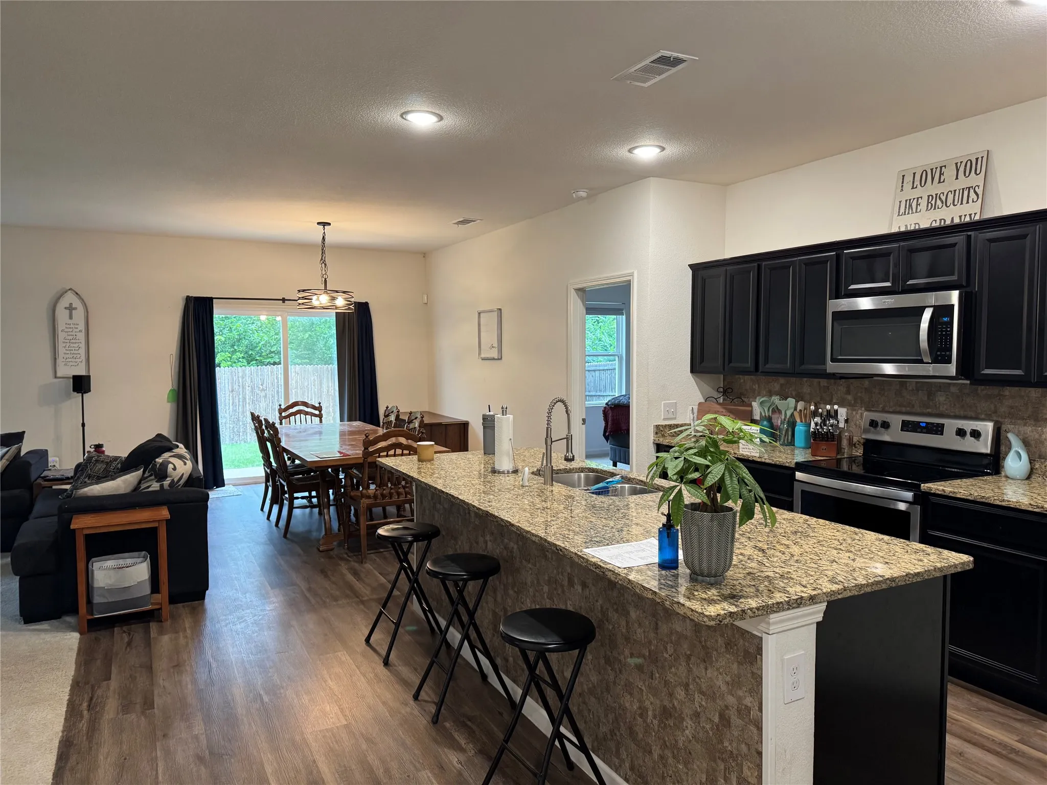 Open-concept kitchen and dining area featuring dark cabinetry, stainless steel appliances, and a granite-finish island with seating