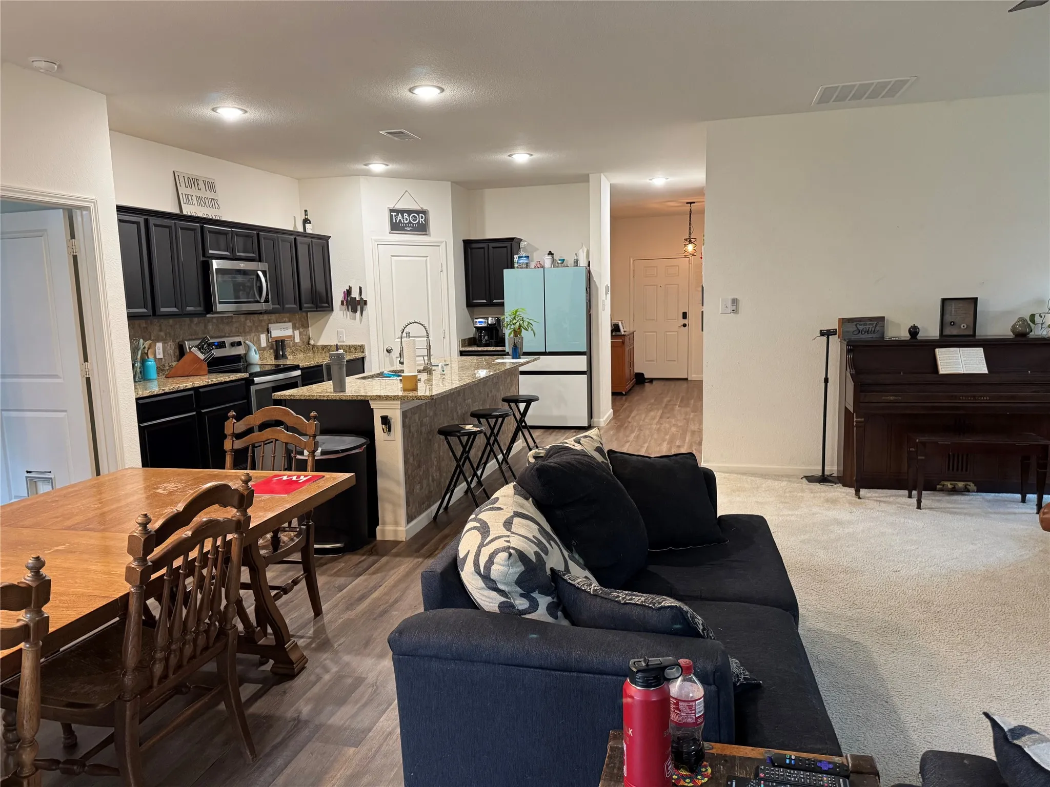Open concept living space featuring a kitchen with dark cabinetry, stainless steel appliances, and a central island with bar seating