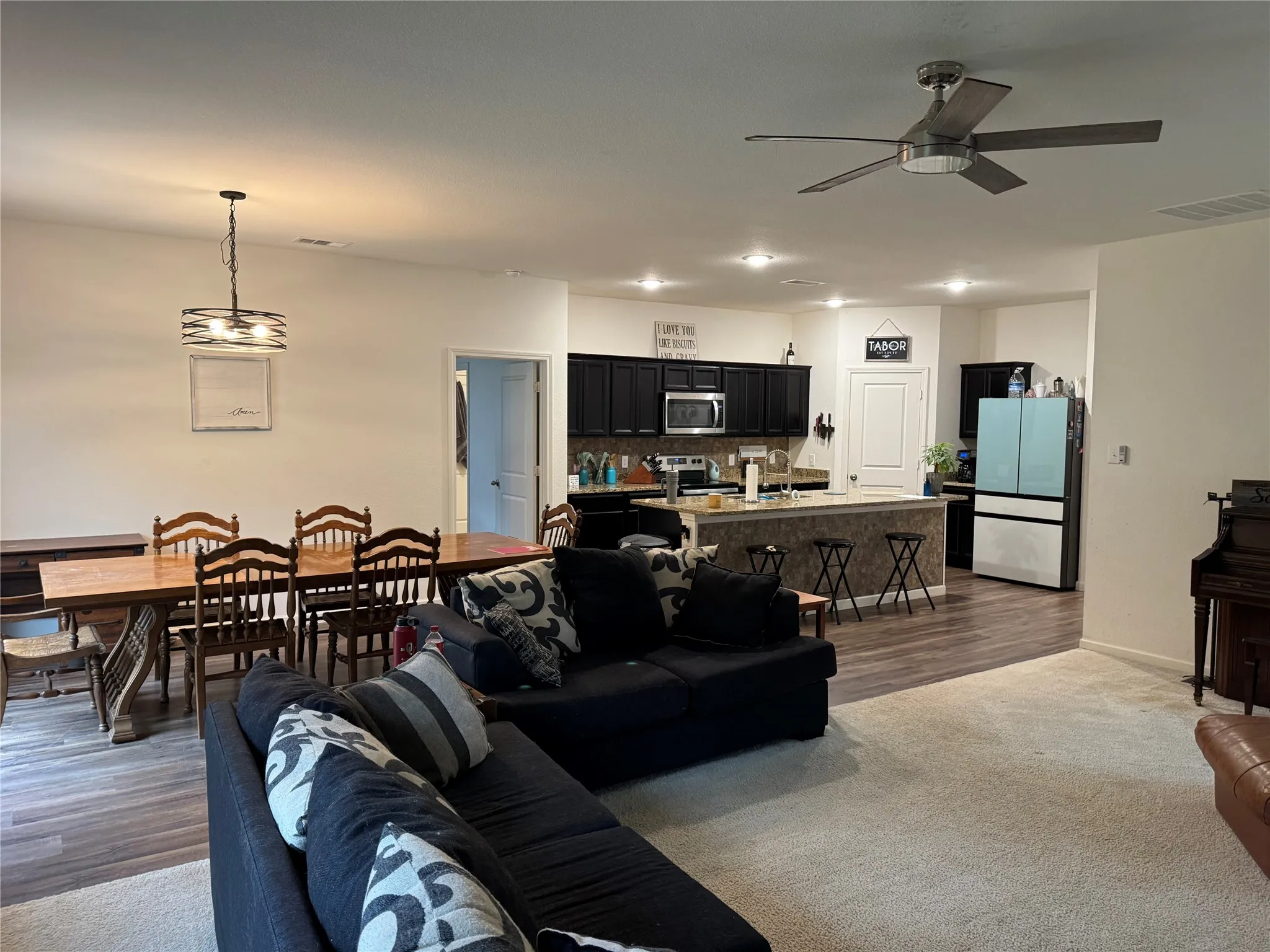 Open-concept living area featuring a kitchen with black cabinetry and light countertops, a dining space with a circular pendant light fixture, and a living area with a ceiling​​‌​​​​‌​​‌‌​‌‌​​​‌‌​‌​‌​‌​​​‌​​ fan