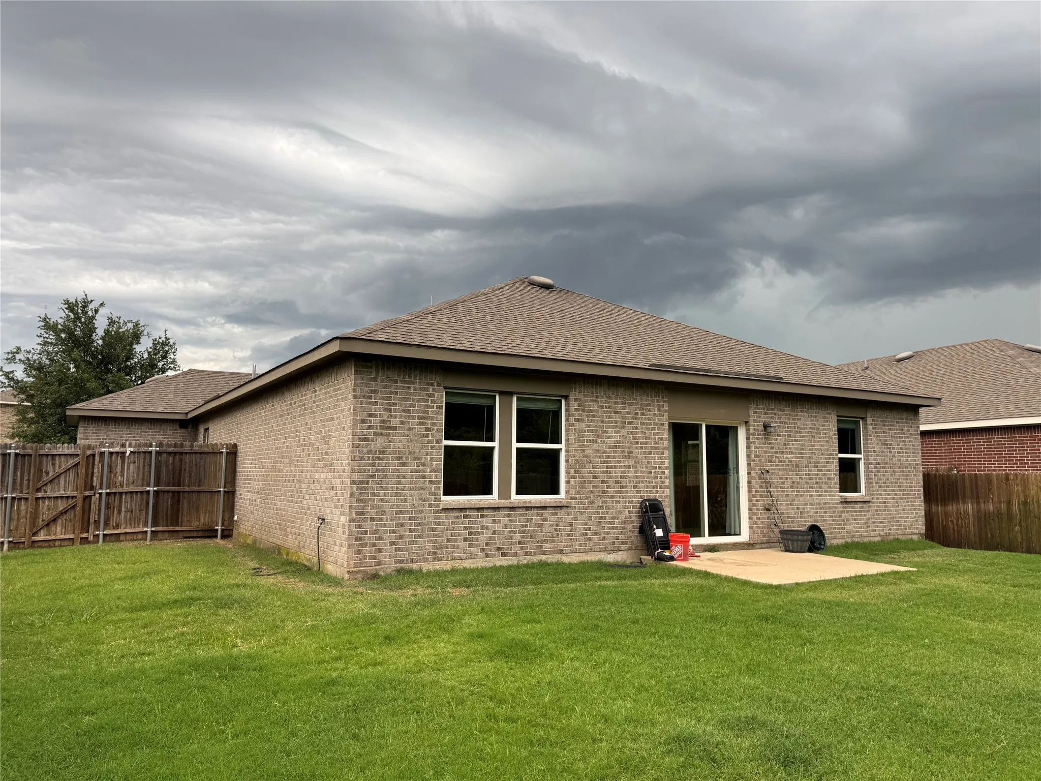 Rear exterior featuring a brick facade, sliding glass patio door, and a concrete patio pad