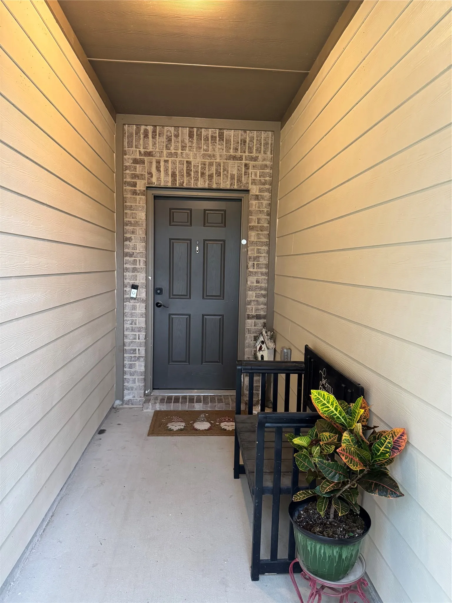 Entryway featuring a dark paneled door framed by brick detailing, light-colored horizontal siding, and a concrete porch