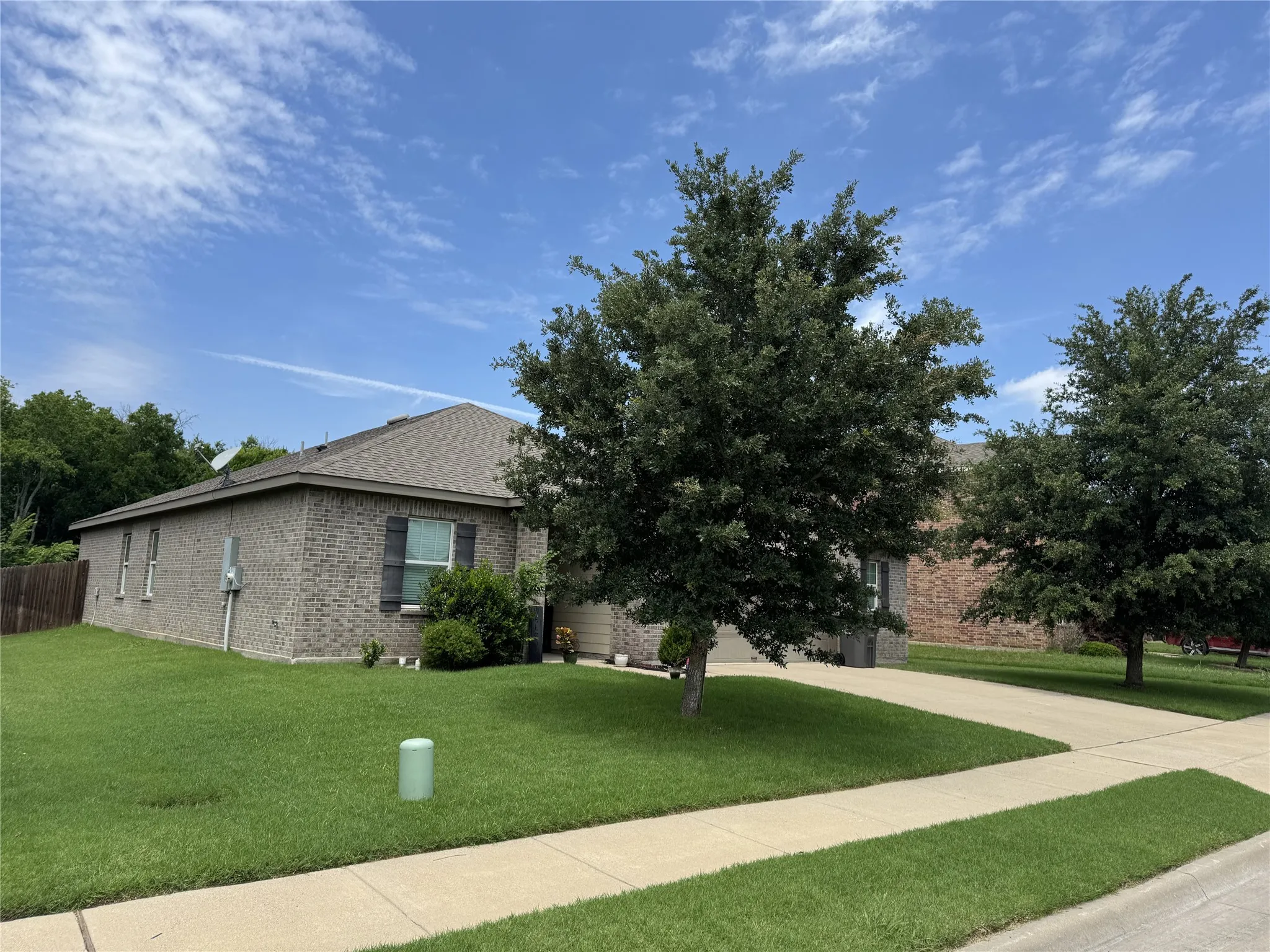 Gray brick exterior with dark shutters, featuring a manicured lawn and mature trees