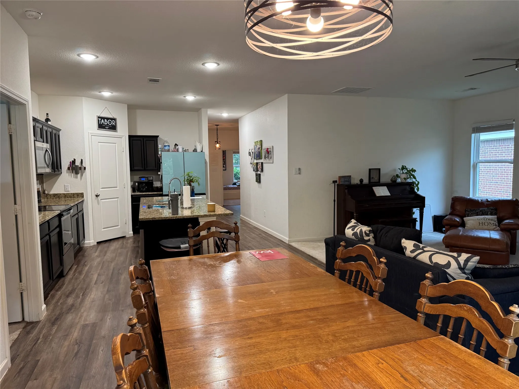 Open-concept living area featuring wood-finish flooring, recessed lighting, and a modern kitchen with dark cabinetry, stainless steel appliances, and granite countertops