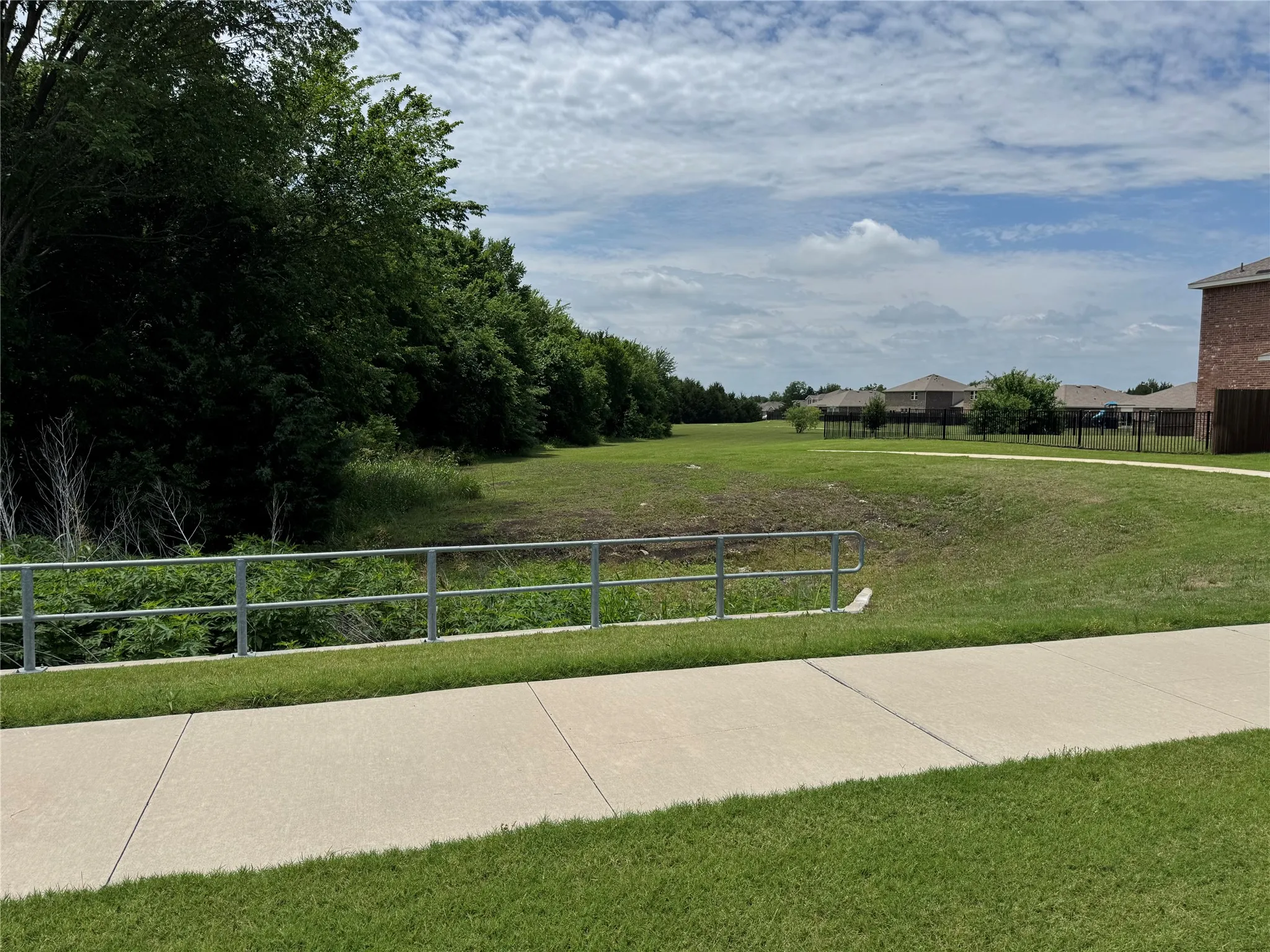 Concrete pathway bordering a grassy area with a metal safety rail