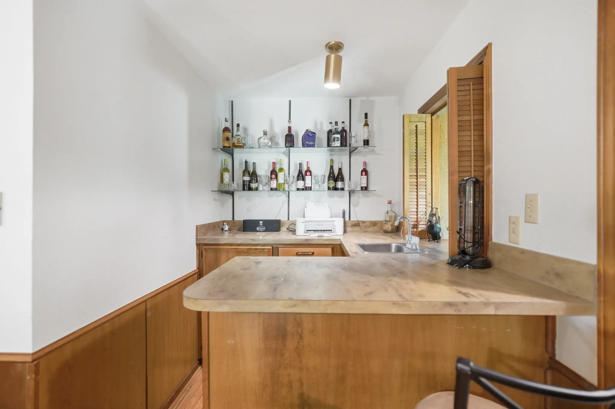 Built-in wet bar featuring a U-shaped countertop, integrated sink, and glass shelving