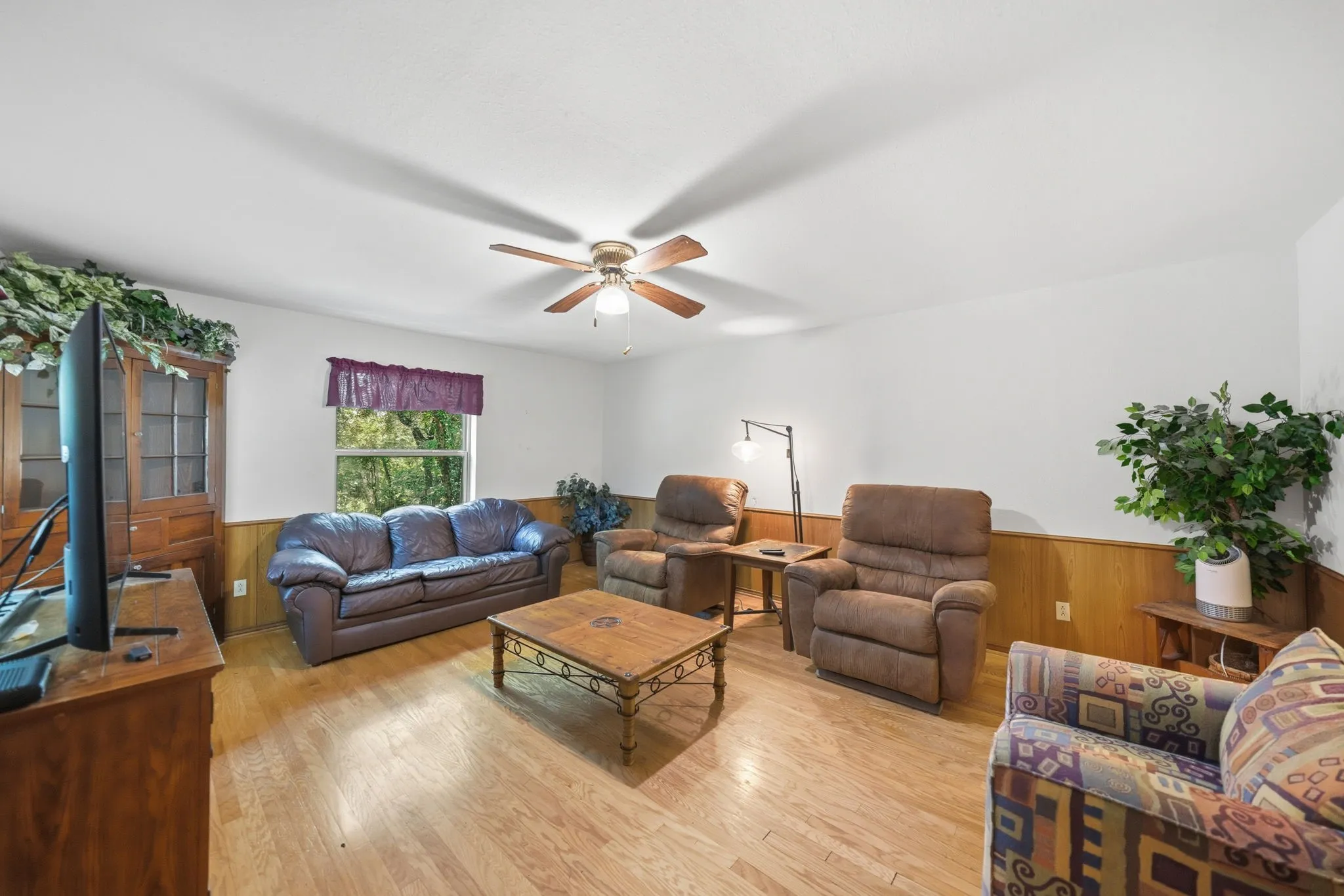Living area featuring wood-finish flooring, white walls, and a wood-paneled wainscoting