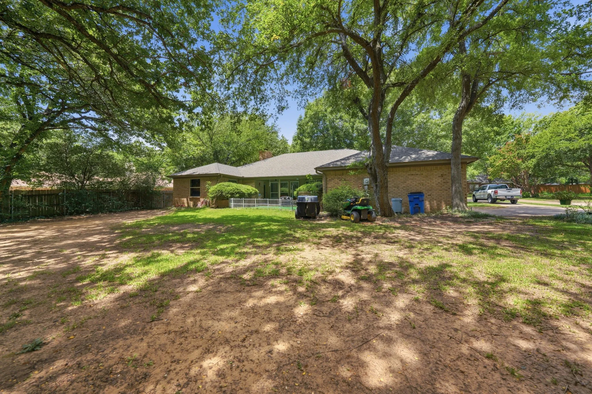 Expansive backyard featuring mature trees, a mix of grass and natural ground cover, and a brick exterior dwelling with a shingled roof