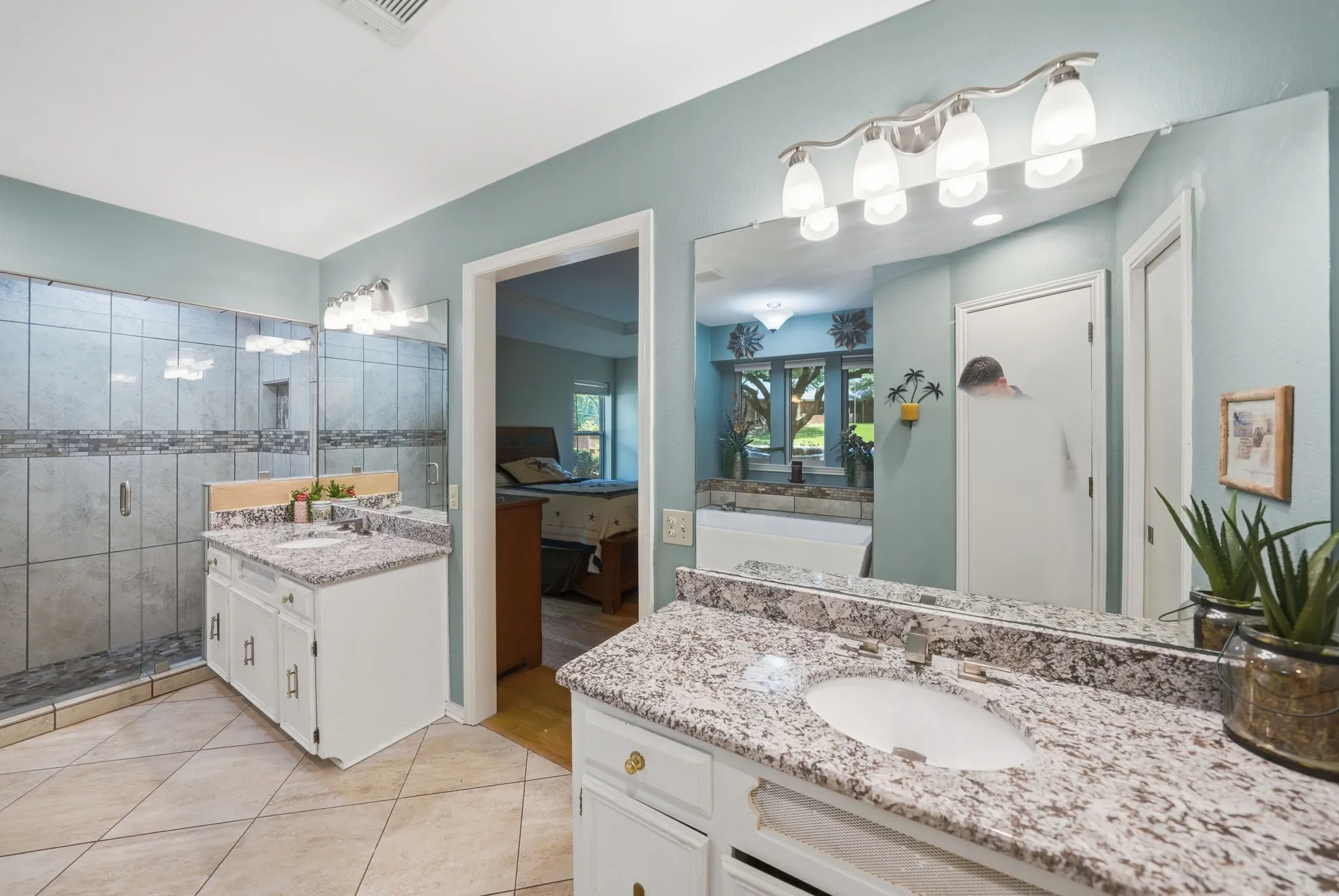 Bathroom featuring dual vanities with granite countertops, integrated sinks, and white cabinetry