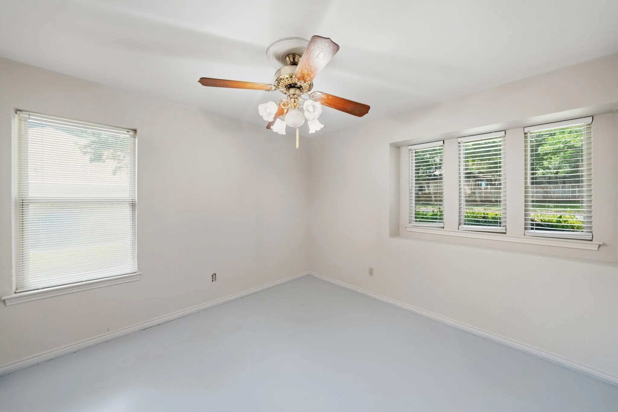 Light-filled room featuring a ceiling fan with light kit, a single window with blinds, and a trio of windows with blinds