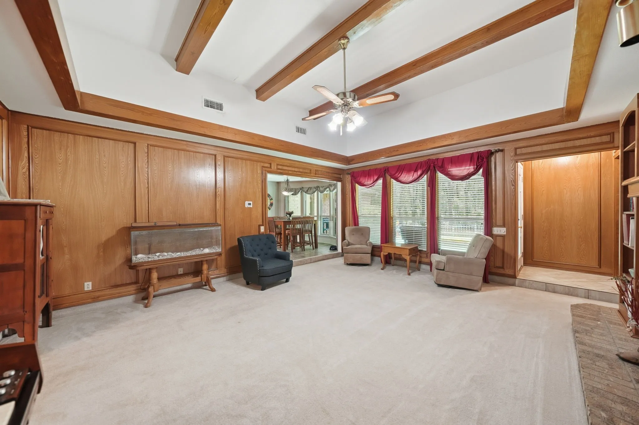 Vaulted ceiling with exposed wood beams, expansive paneling, large picture windows, and ceiling fan fixture