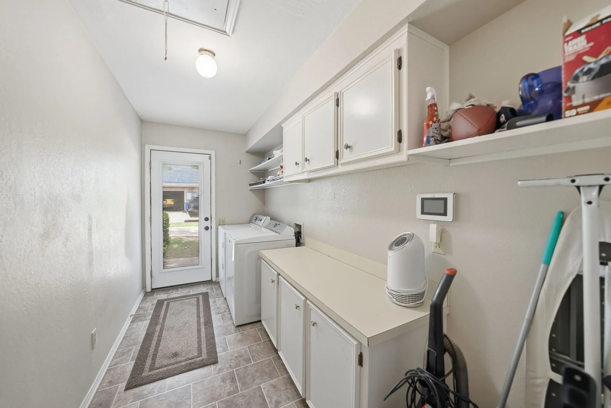 Laundry area featuring gray tile flooring, white cabinetry, integrated countertop space, and a glass-paneled exterior door
