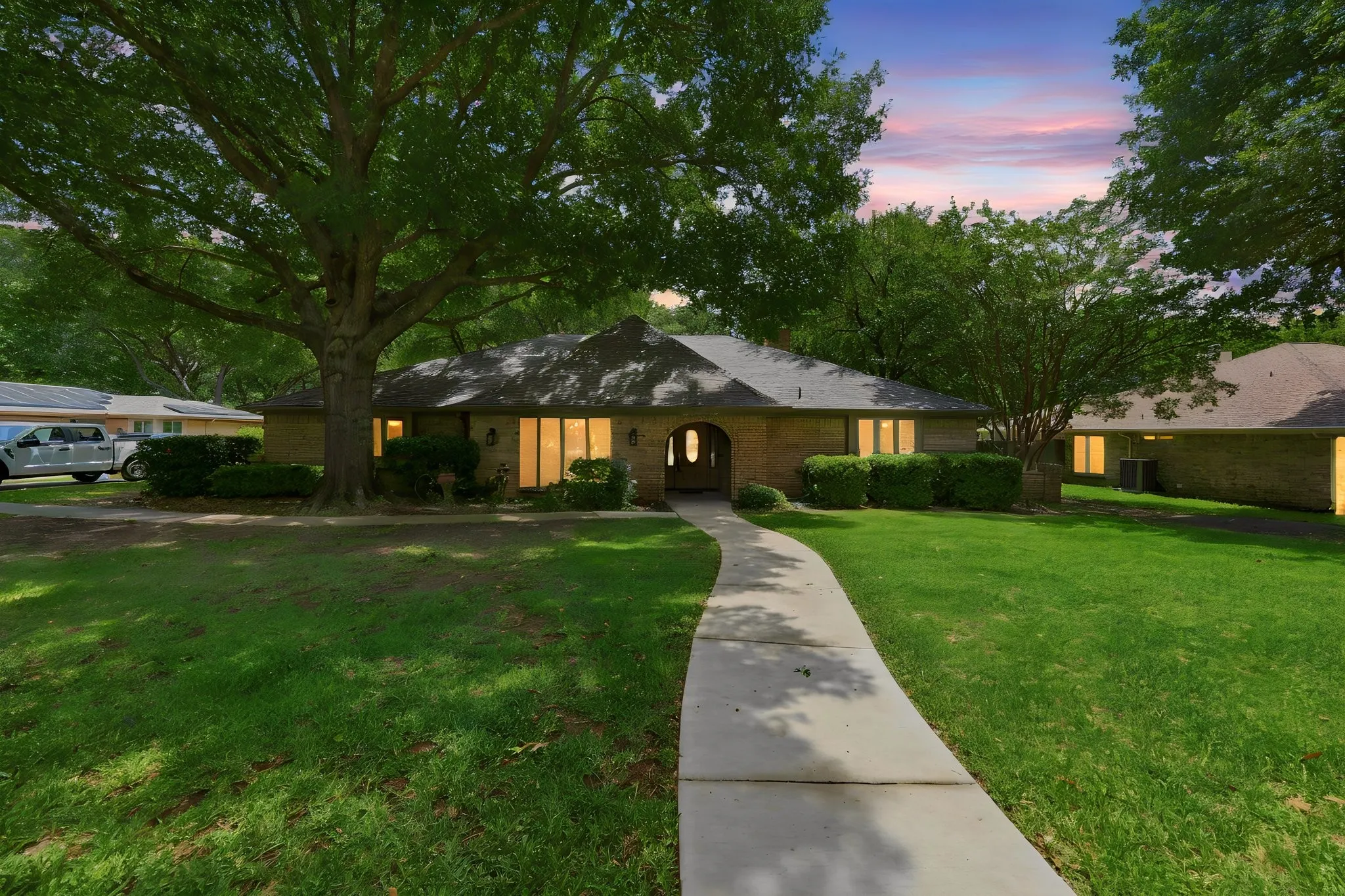 Brick exterior with a prominent arched entry, surrounded by mature trees and manicured shrubbery
