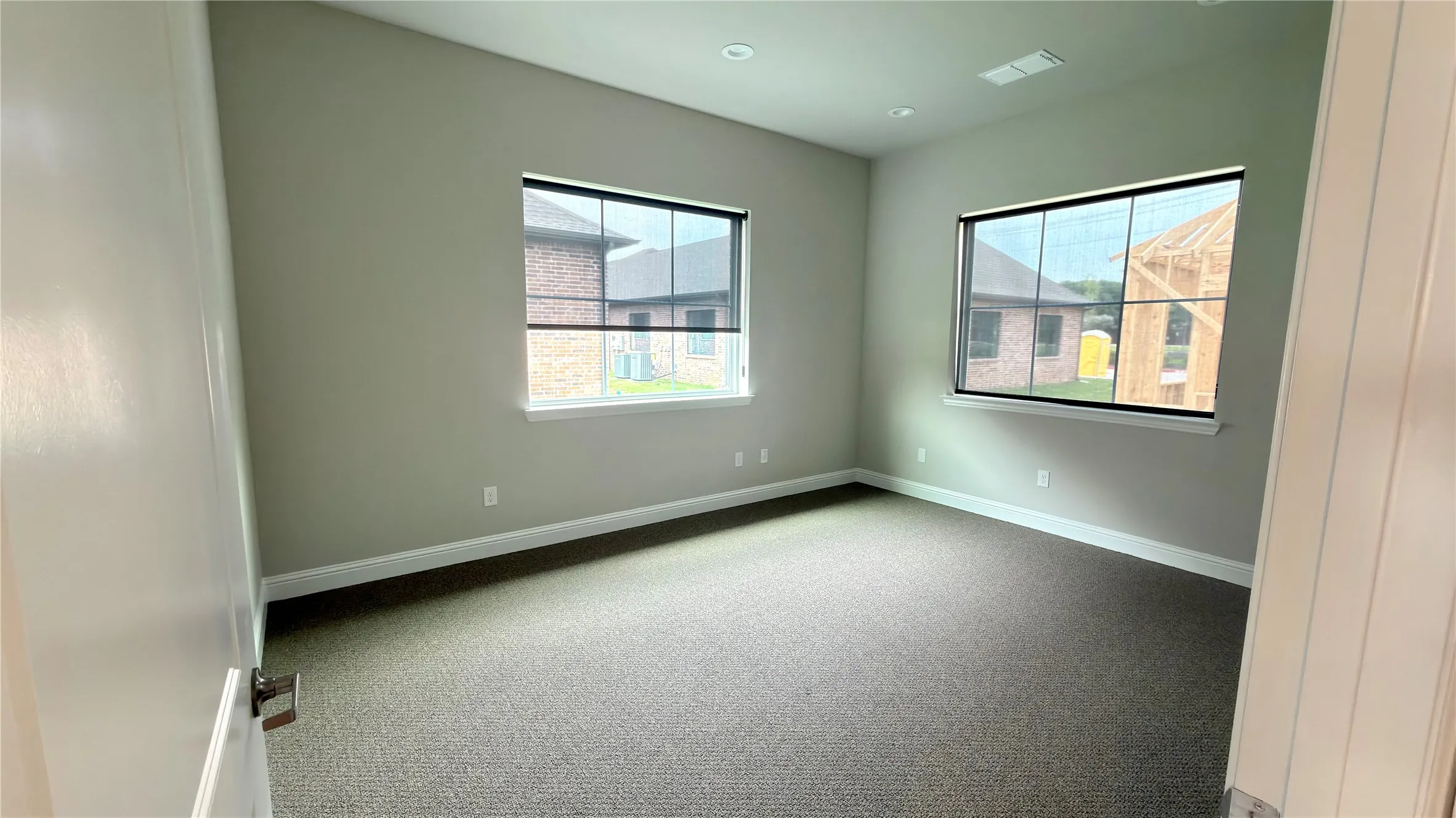 Spacious room featuring neutral carpeting, two large windows with window treatments, and high ceilings
