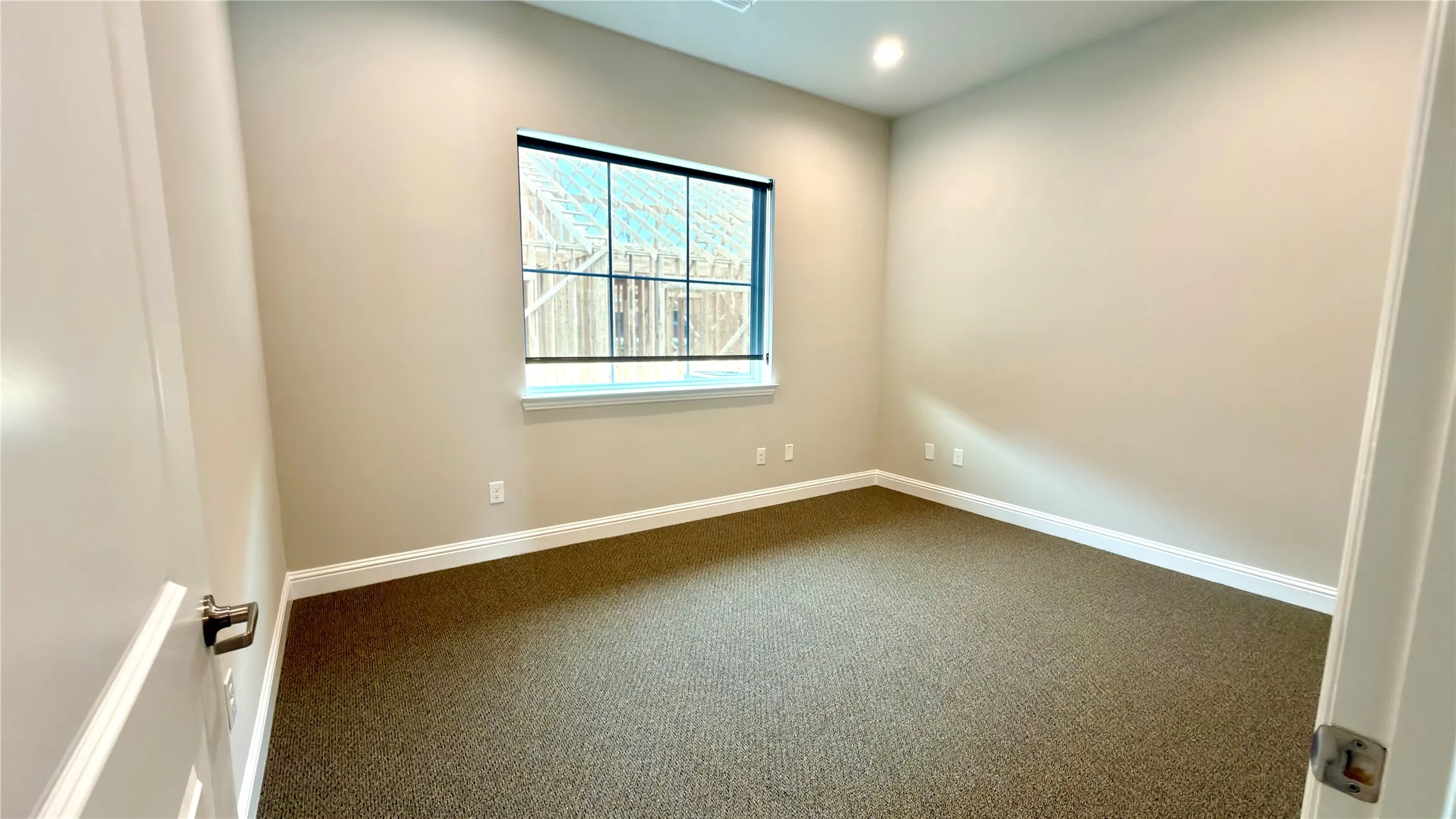 Spacious room featuring neutral wall tones, modern recessed lighting, a large window with gridded panes, and durable carpeting