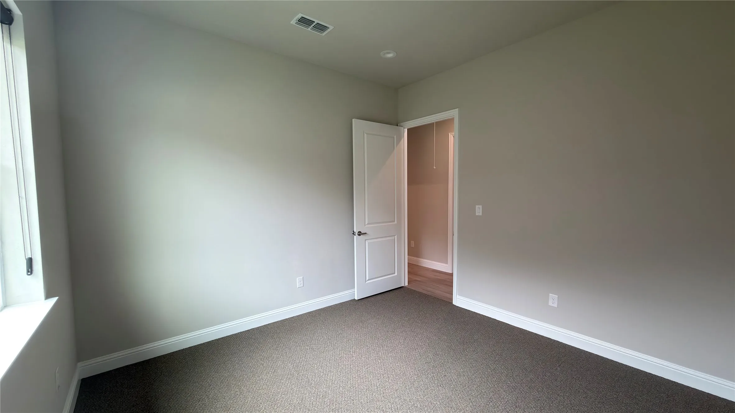 Neutral-toned room with plush carpeting, white trim, recessed lighting, and a window providing natural illumination