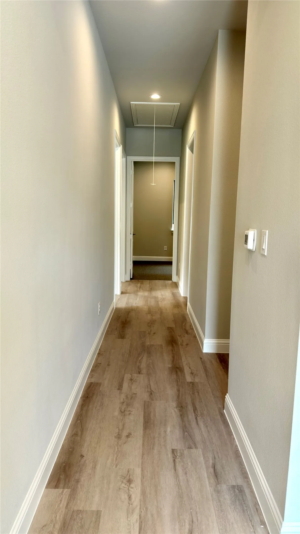 Hallway featuring wood-finish flooring, recessed lighting, and crisp white baseboards