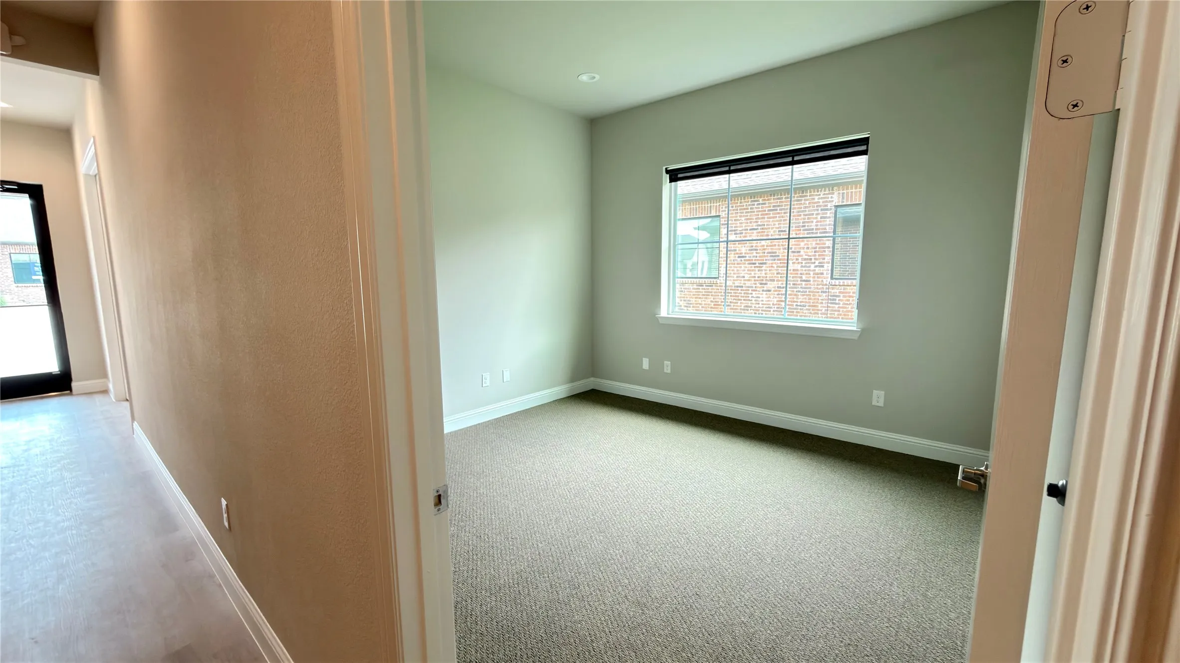 Carpeted room featuring a large window with horizontal blinds, light green painted walls, and white baseboards