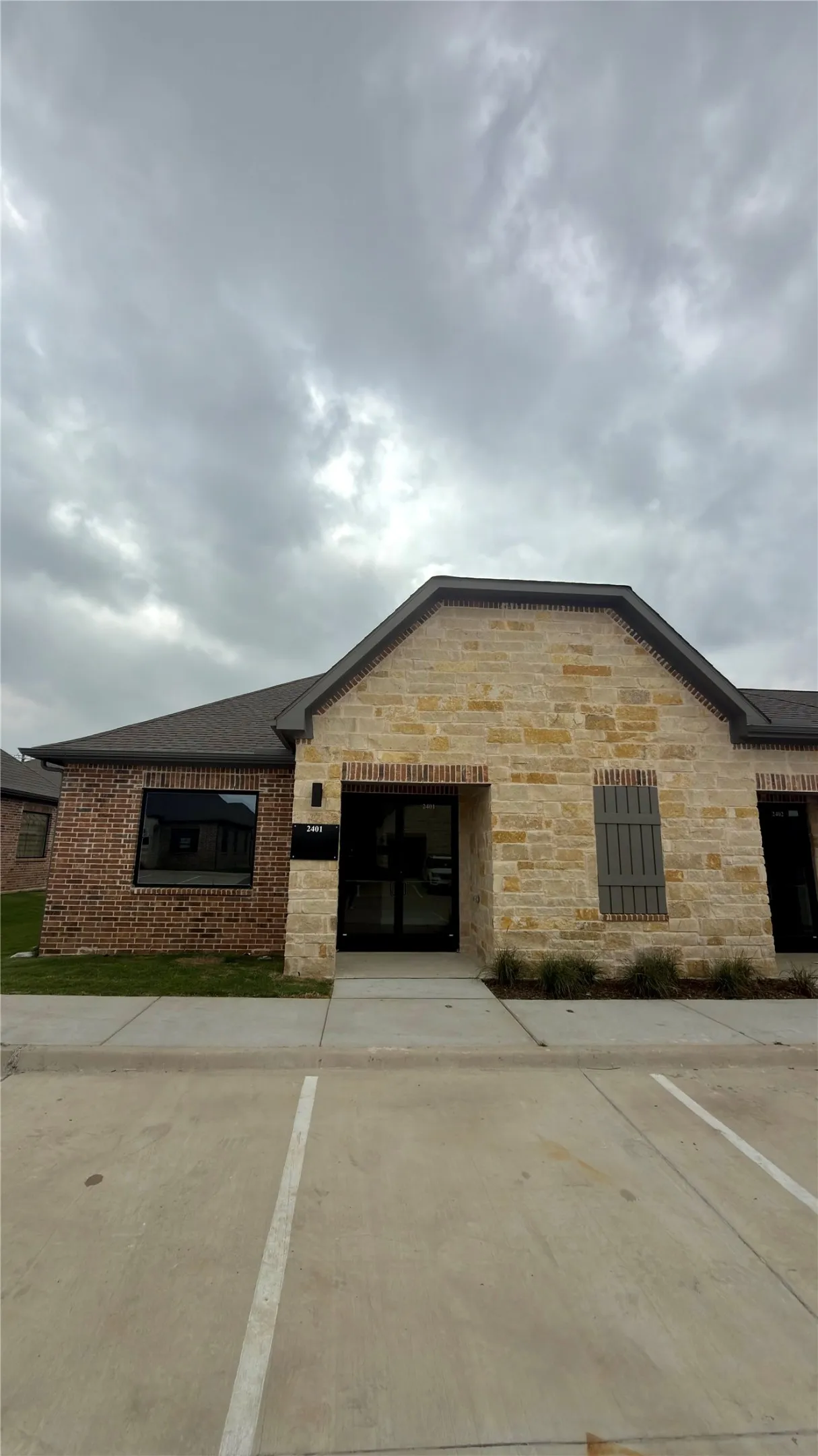 Exterior featuring a combination of brick and stone masonry, a dark shingle roof, a prominent front entrance with double glass doors, a window with black trim, and decorative exterior shutters