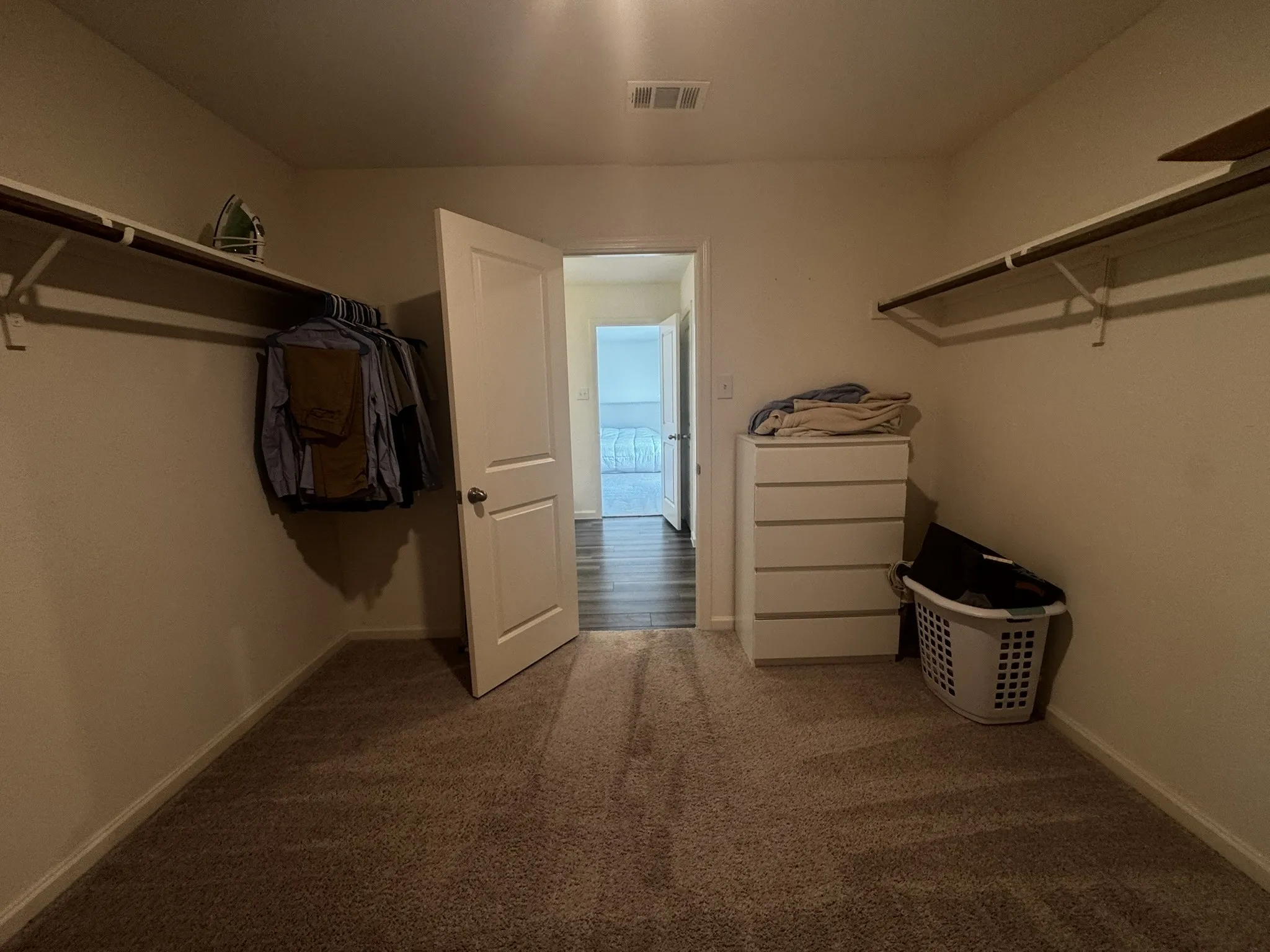 Spacious walk-in closet featuring plush carpet flooring, white walls, and built-in shelving with hanging rods on both sides